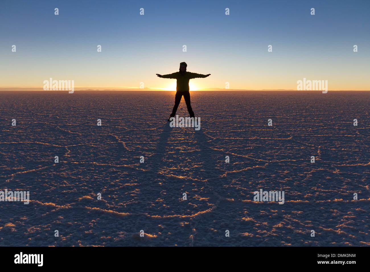 Persona standiing davanti al sole nascente in Salar de Uyuni, Bolivia Foto Stock