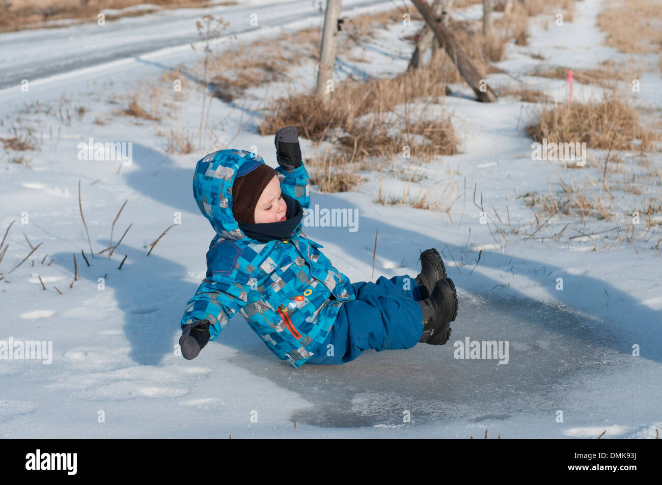 Un bambino scivola su una pozzanghera ghiacciata Foto Stock