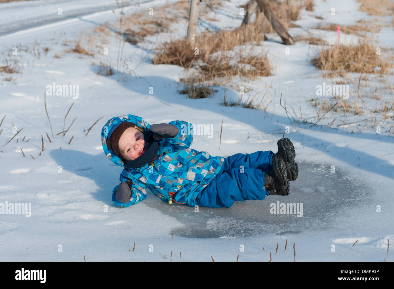 Un bambino scivola su una pozzanghera ghiacciata Foto Stock