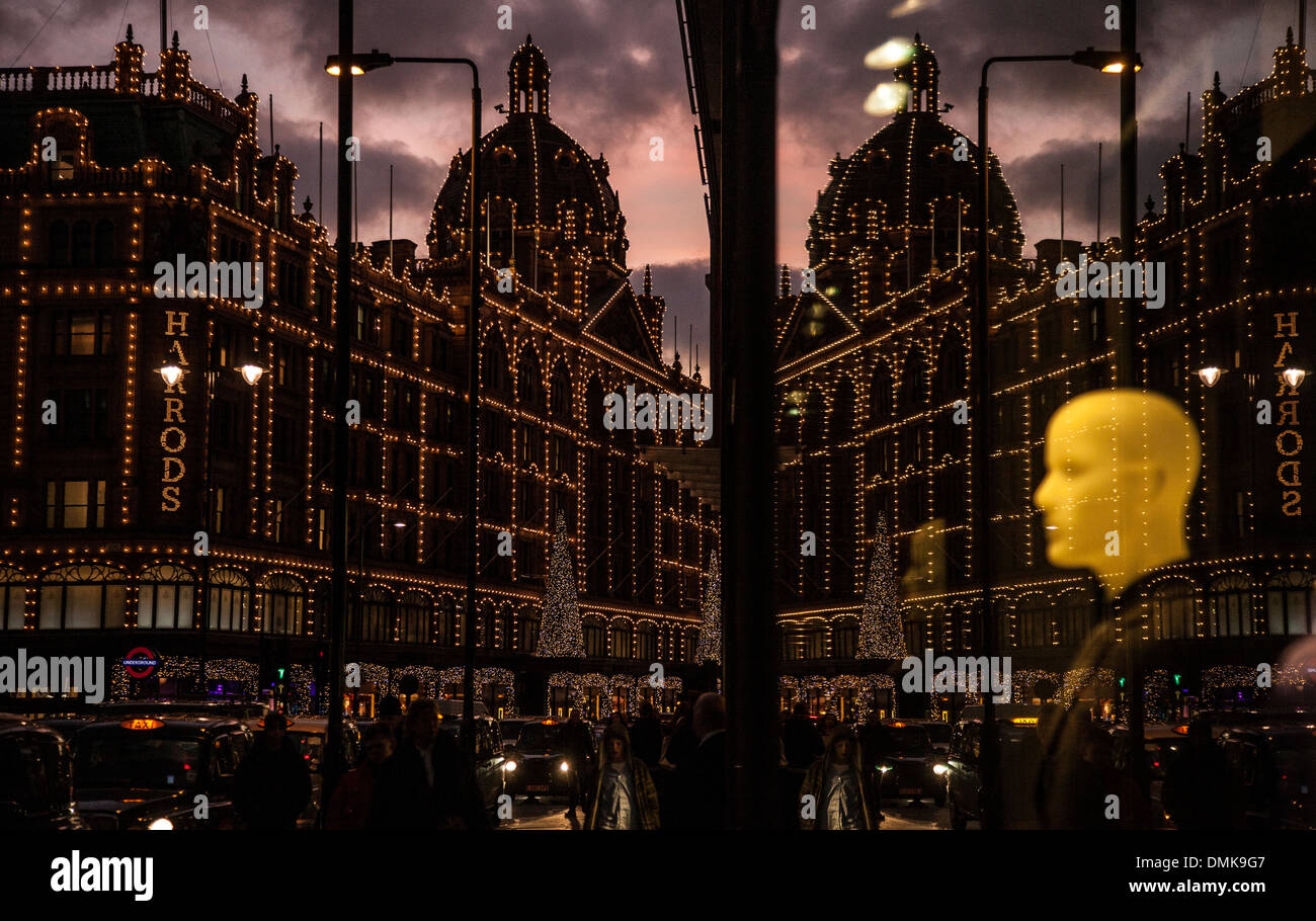 I grandi magazzini Harrods, Knightsbridge, Londra con le luci di Natale sul riflesso in un vicino negozio finestra. Foto Stock