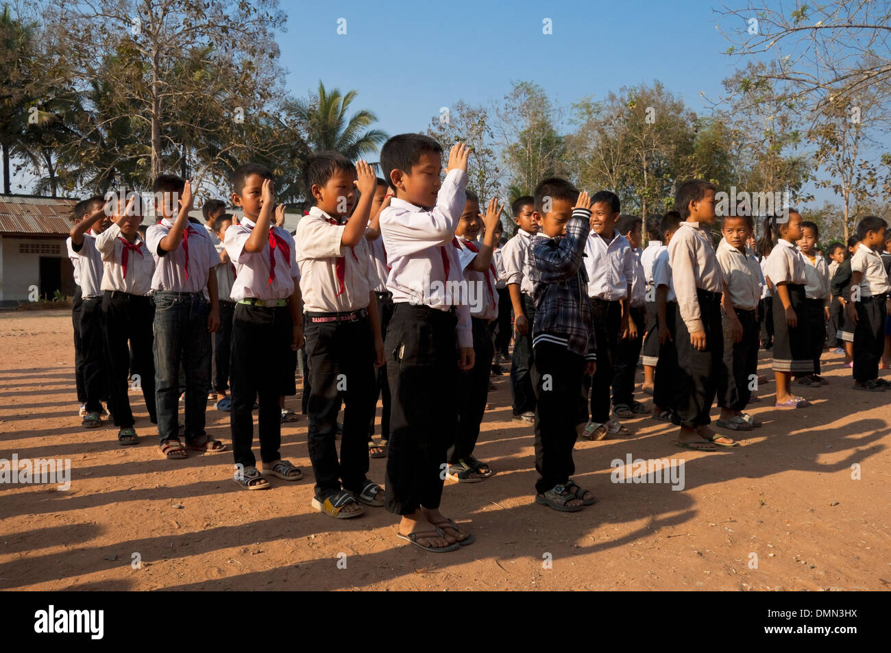 Vista orizzontale della scuola bambini salutando e cantando insieme durante la loro bandiera il sollevamento ad una scuola in Laos. Foto Stock