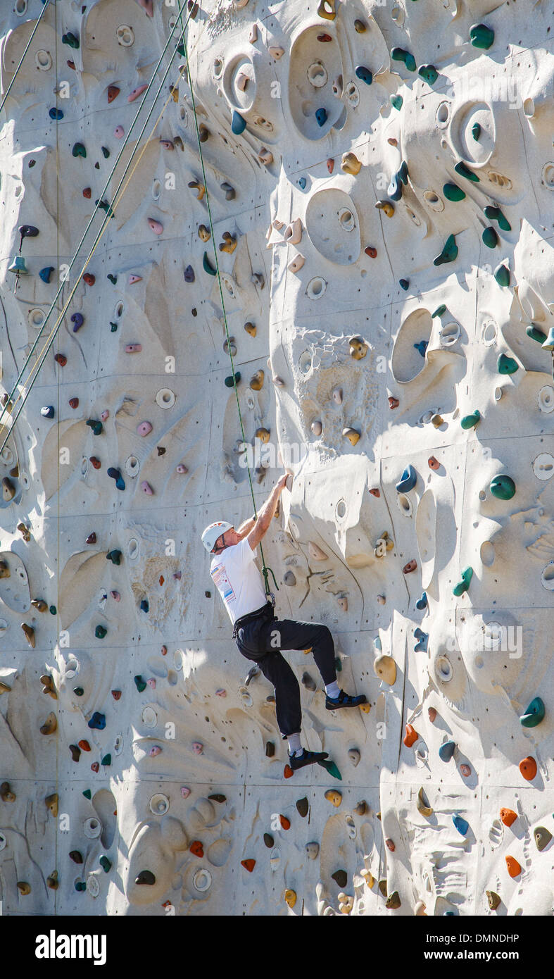 Un uomo più anziano arrampicata su una parete di roccia con cavi di sicurezza e casco Foto Stock