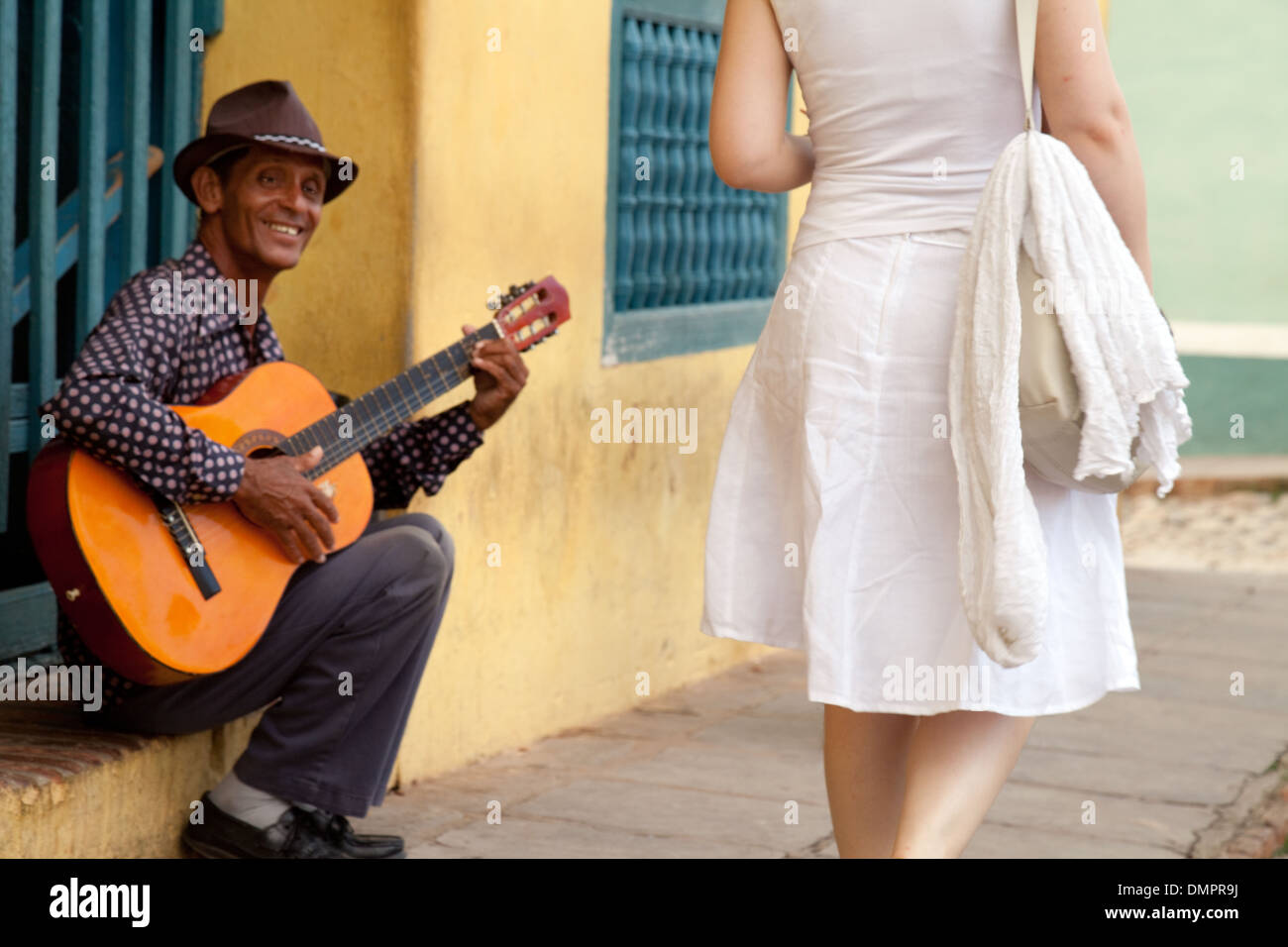 Un chitarrista giocando in questa scena di strada come una donna cammina passato - La cultura cubana in Trinidad, Cuba, Caraibi, America Latina Foto Stock