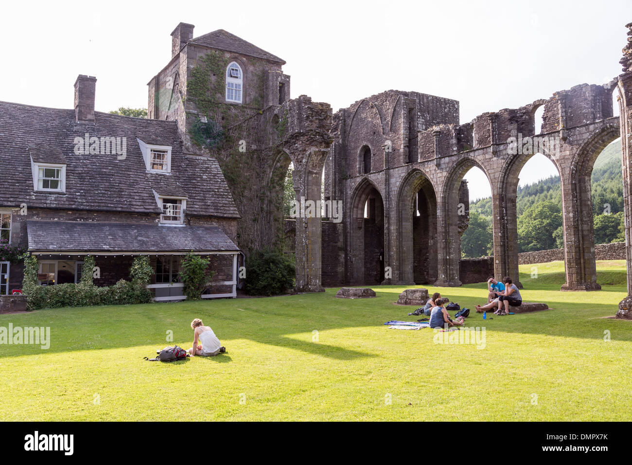 La gente seduta su erba nel sole a Llantony Priory rovine, vale di Ewas, Montagna Nera, Wales, Regno Unito Foto Stock