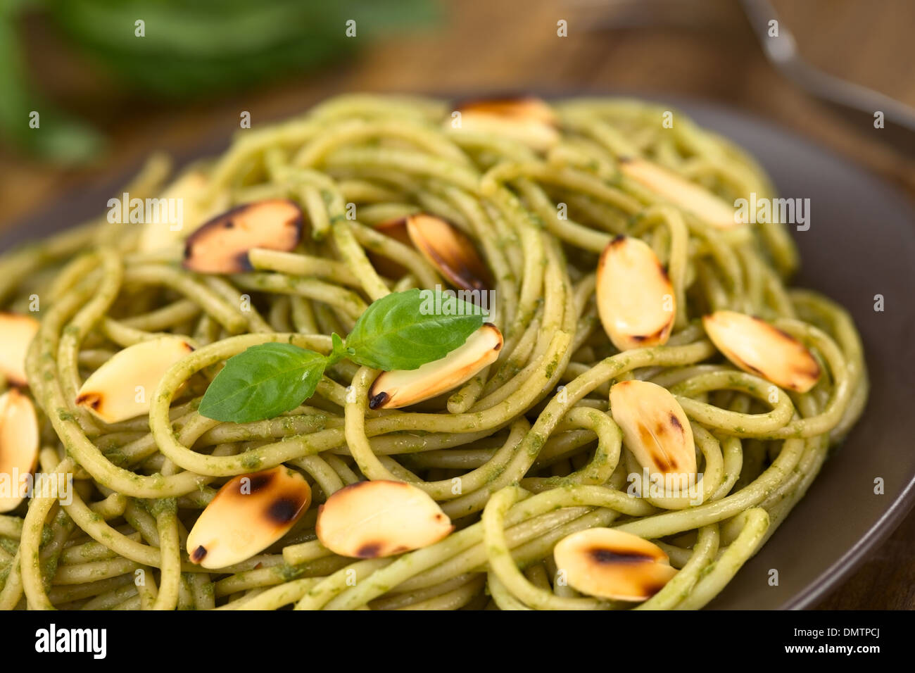 Pasta al pesto fatta di basilico e spinaci guarnito con mandorle tostate servito su una piastra marrone Foto Stock