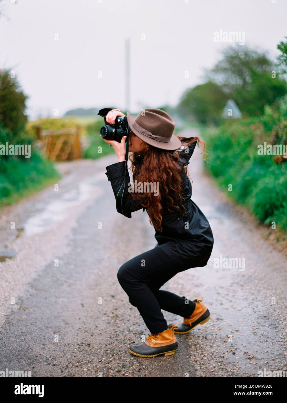 Una donna accovacciata a prendere una fotografia su una strada di campagna. Foto Stock