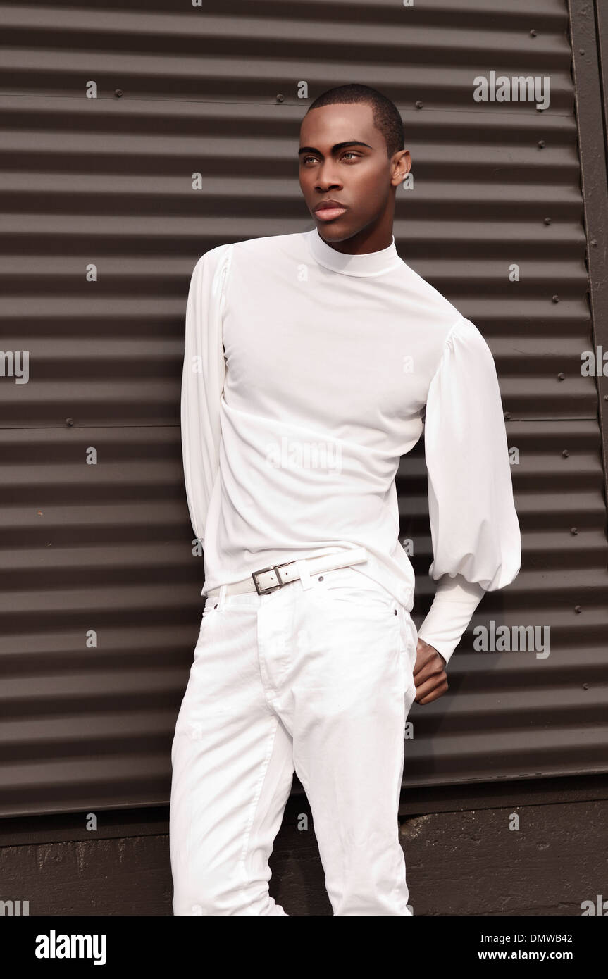 Un bel uomo nero, African American maschio modello vestito con un abito bianco in posa contro il metallo parete nera. Foto Stock