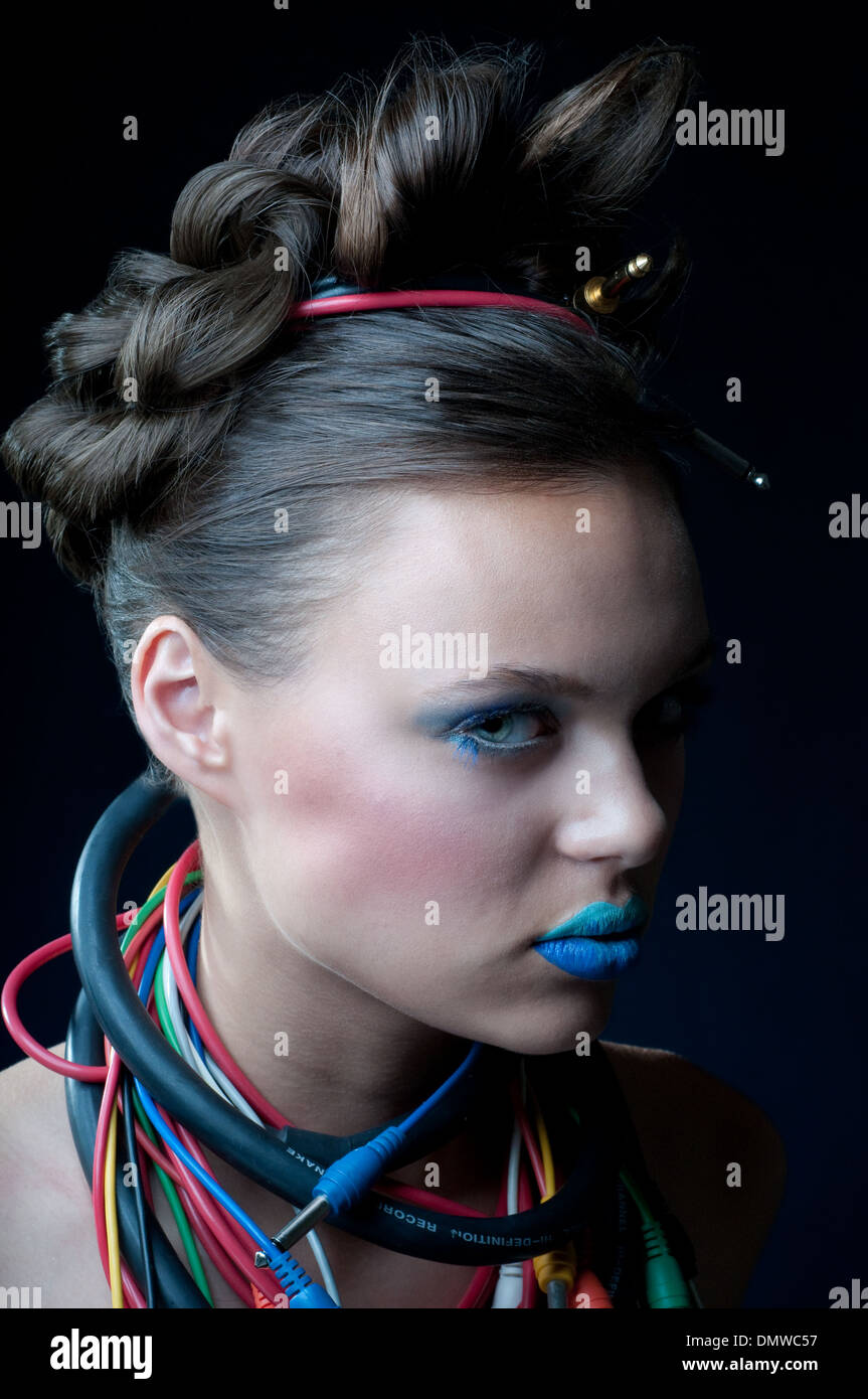 Una giovane e bella donna con ombre blu trucco, fissando in telecamera con il cavo elettrico, la musica i cavi avvolti intorno al suo collo. Foto Stock