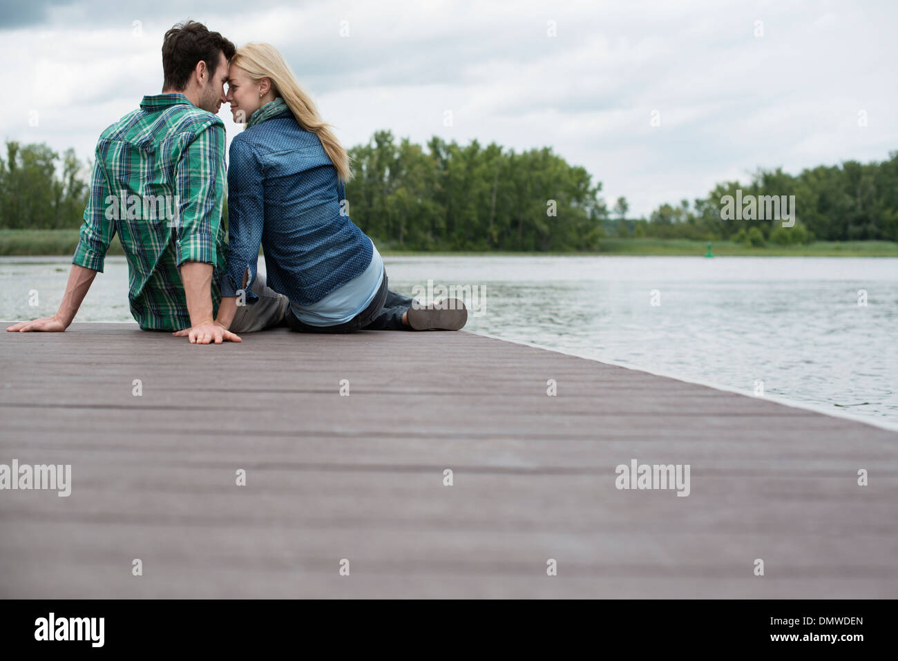 Un uomo e una donna seduta su un molo da un lago. Foto Stock