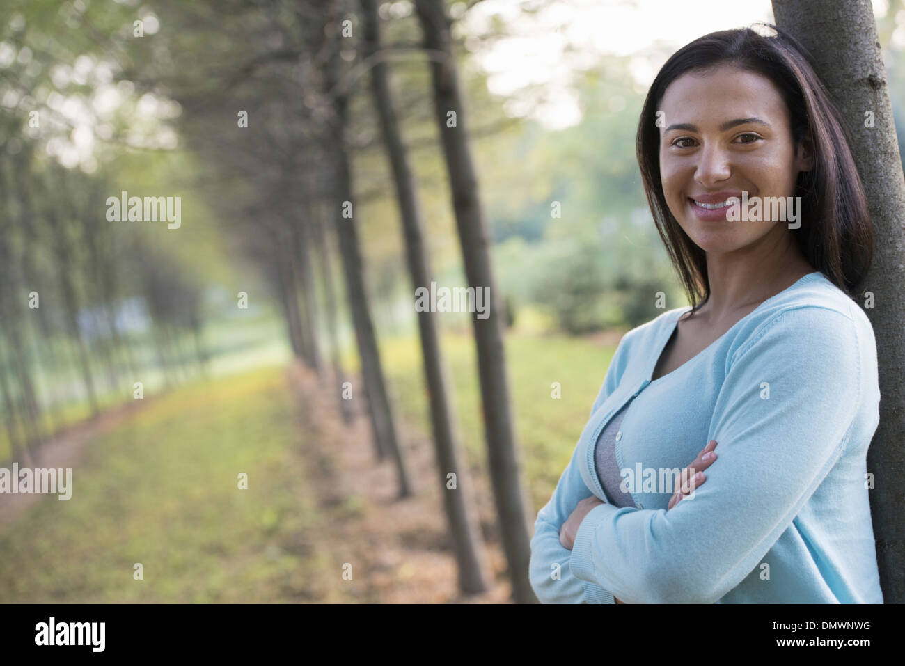 Una donna con le braccia incrociate appoggiata contro un albero. Foto Stock