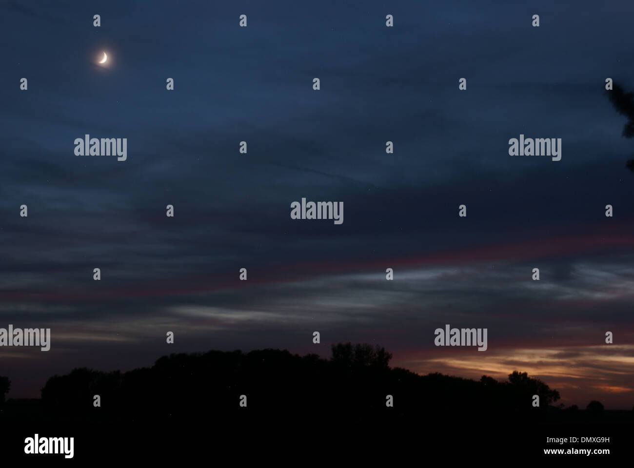 Nuvoloso Tramonto con la falce di luna Foto Stock