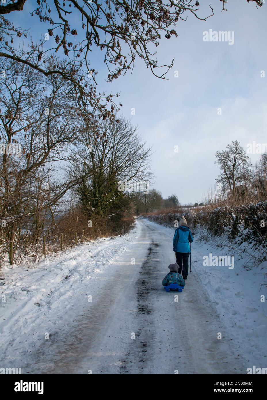 Una madre tirando il suo figlio in una slitta su una corsia nevoso in Cotswolds Foto Stock