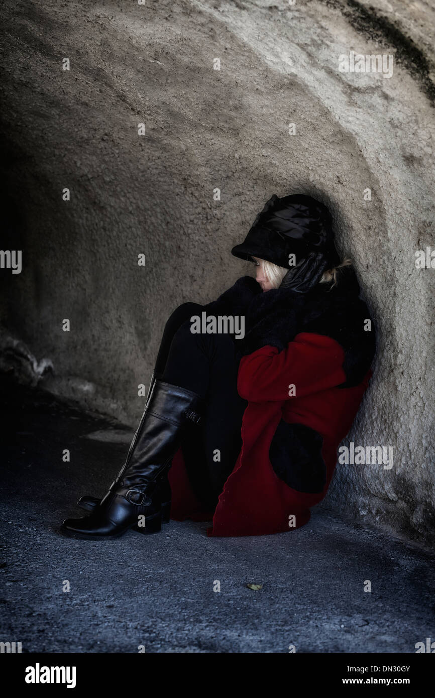 Una donna in un rivestimento di colore rosso è seduto in un buio del tunnel Foto Stock