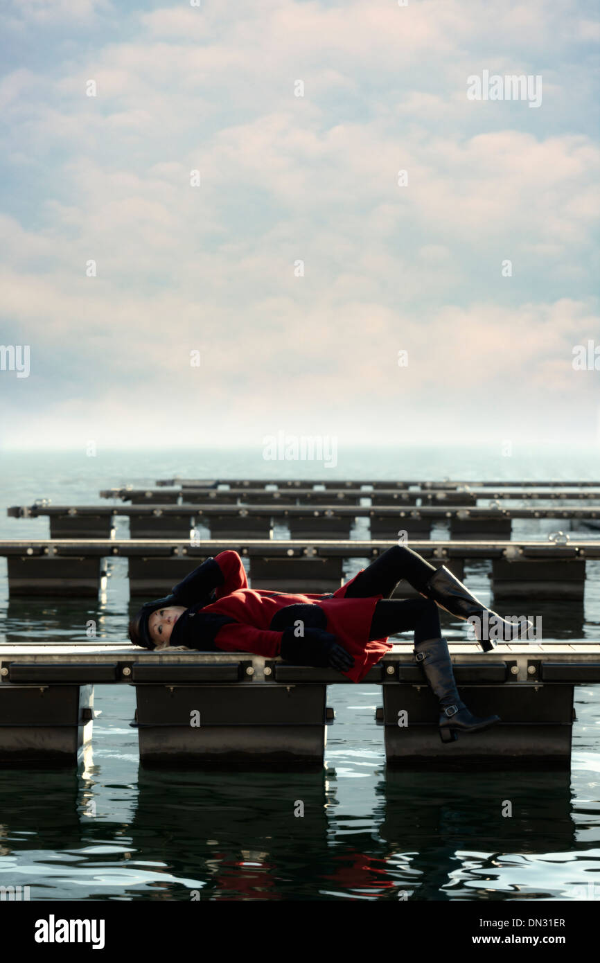 Una donna in un rivestimento di colore rosso è sdraiato su un molo Foto Stock