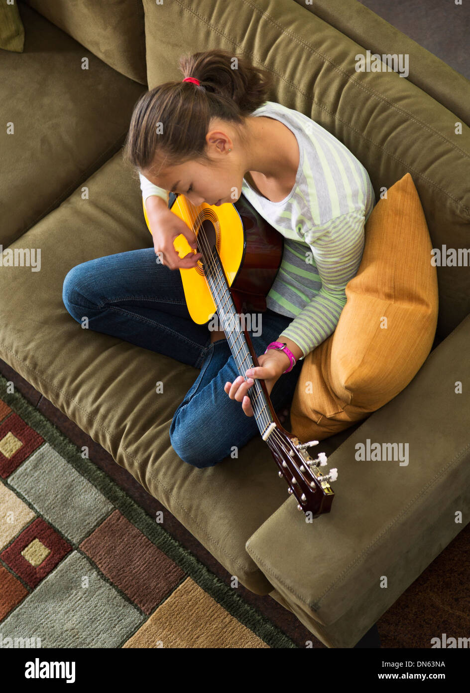 Razza mista ragazza praticando la chitarra su un divano Foto Stock