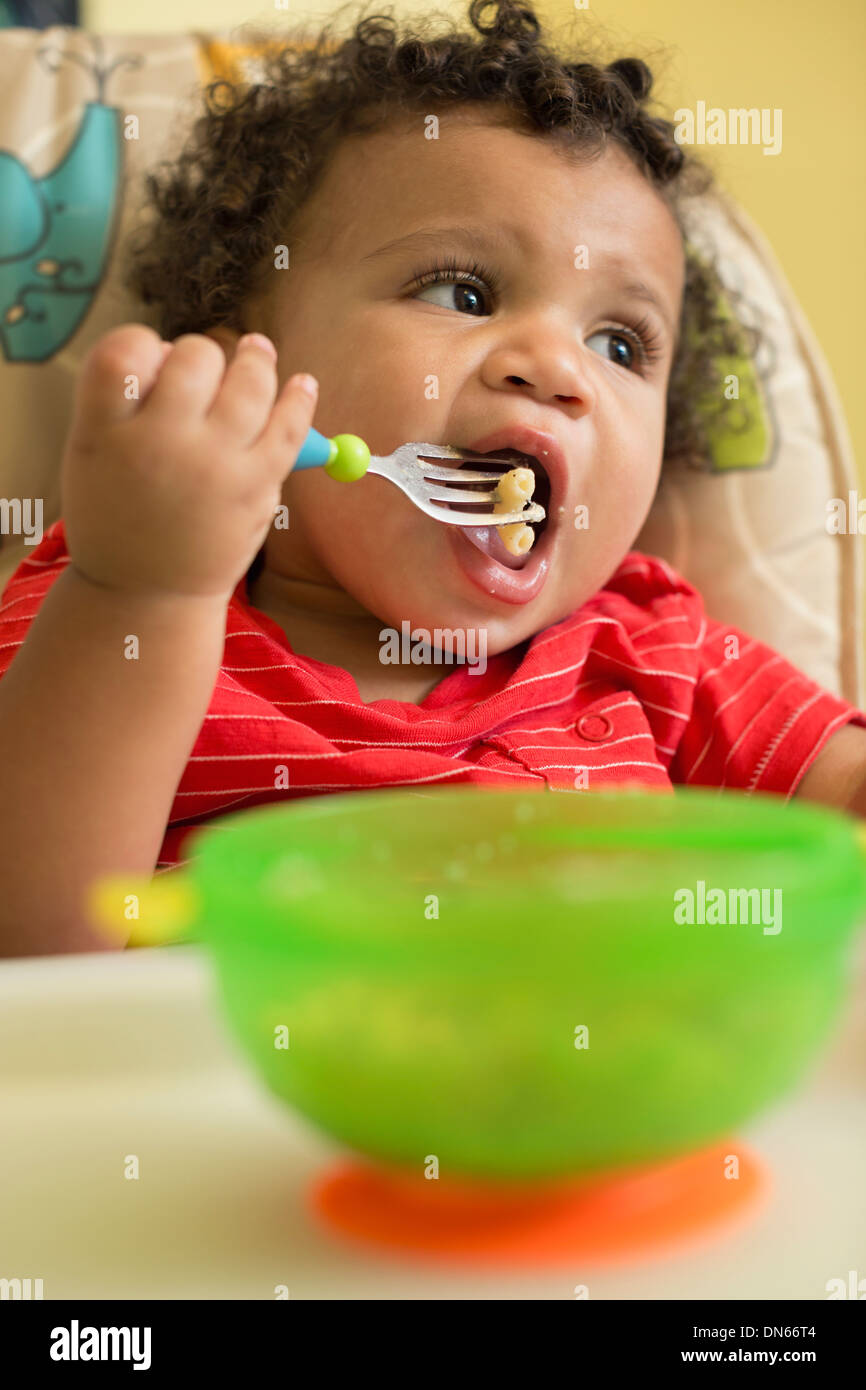 Razza mista toddler boy eating in sedia alta Foto Stock