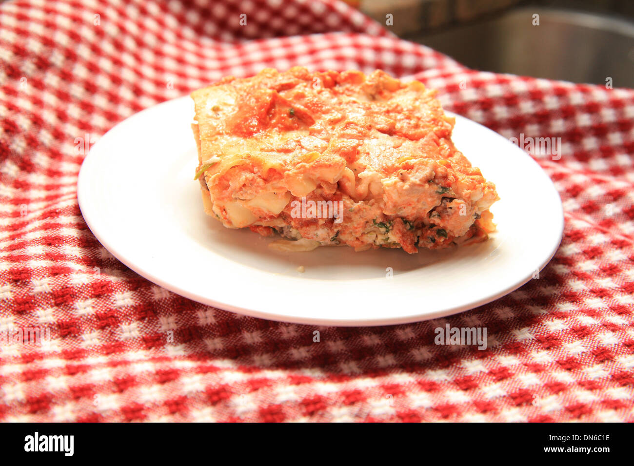 Una fetta di carne fatti in casa lasagne su una piastra bianca con una bottiglia di vino rosso in background Foto Stock