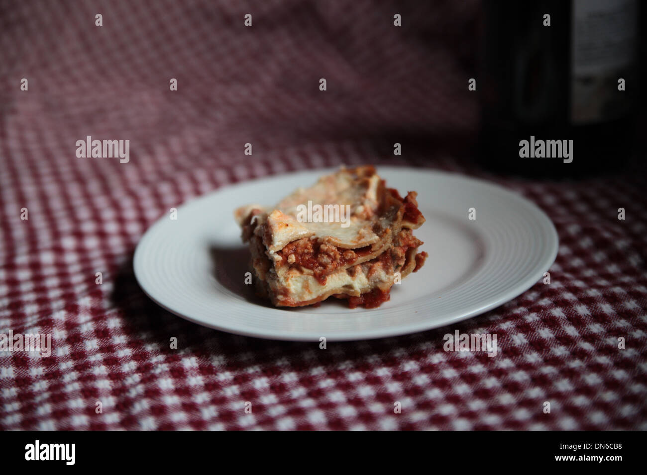 Una fetta di carne fatti in casa lasagne su una piastra bianca con una bottiglia di vino rosso in background Foto Stock