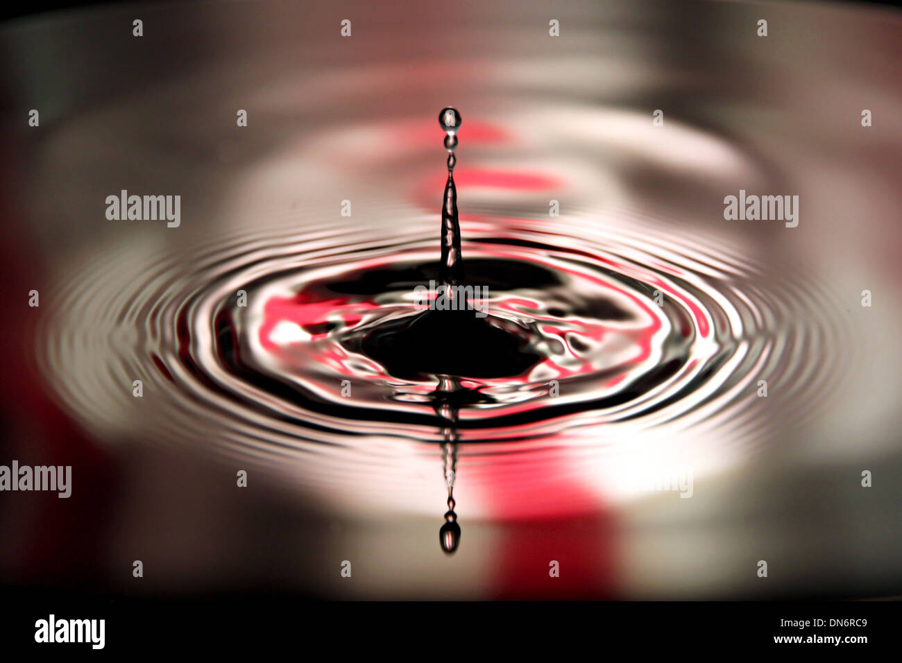 Gocce d'acqua causano la forma su sfondo rosso. Foto Stock