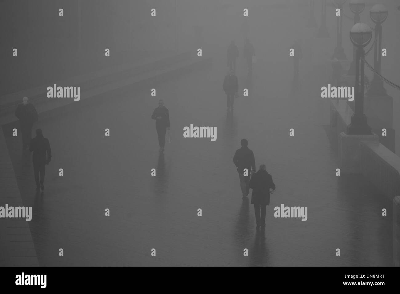 Stagliano figura camminando lungo il Tamigi nella nebbia le loro ombre riflesse sul pavimento bagnato Foto Stock