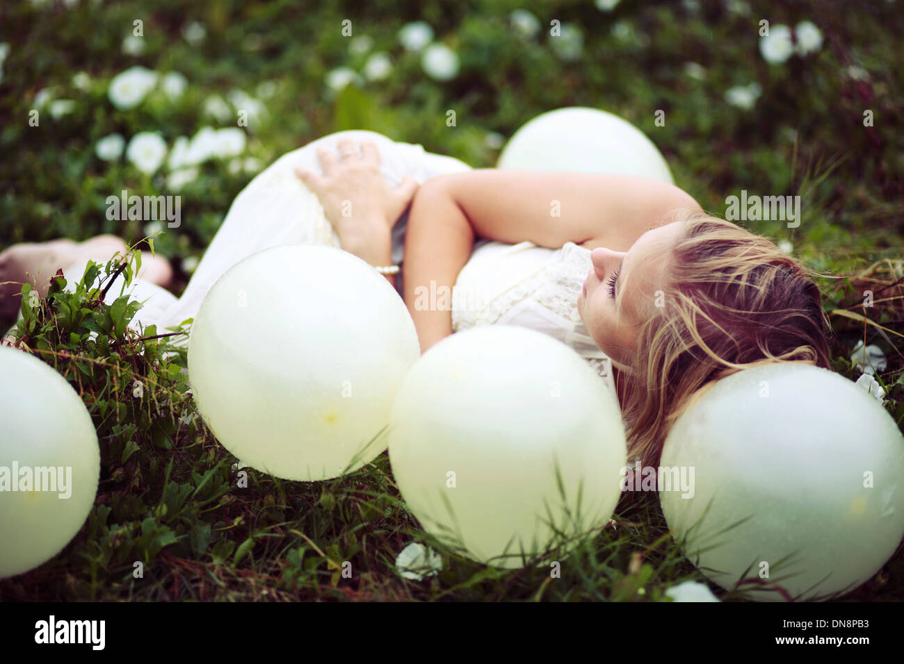 Giovane donna sdraiata su un prato tra palloncini Foto Stock