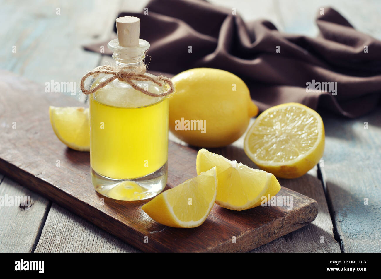 Olio di limone in una bottiglia di vetro con limone fresco su sfondo di legno Foto Stock