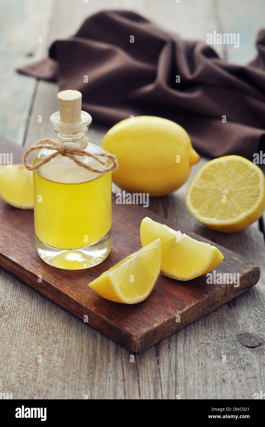Olio di limone in una bottiglia di vetro con limone fresco su sfondo di legno Foto Stock