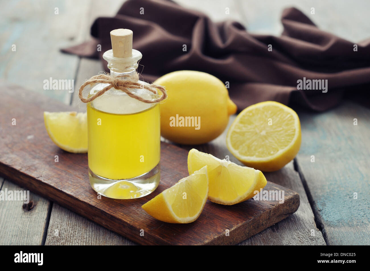 Olio di limone in una bottiglia di vetro con limone fresco su sfondo di legno Foto Stock