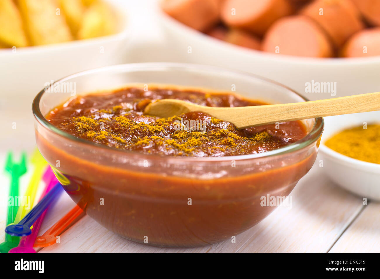 Curry ketchup salsa fatta immergere le salsicce fritte e patatine fritte servite in recipiente di vetro con il cucchiaio di legno Foto Stock