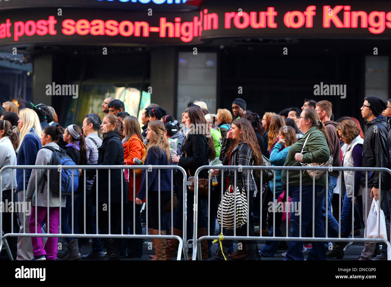 Una grande folla di persone che camminano lungo un marciapiede affollato e barricato in Times Square con un marquee di notizie ticker sopra Foto Stock