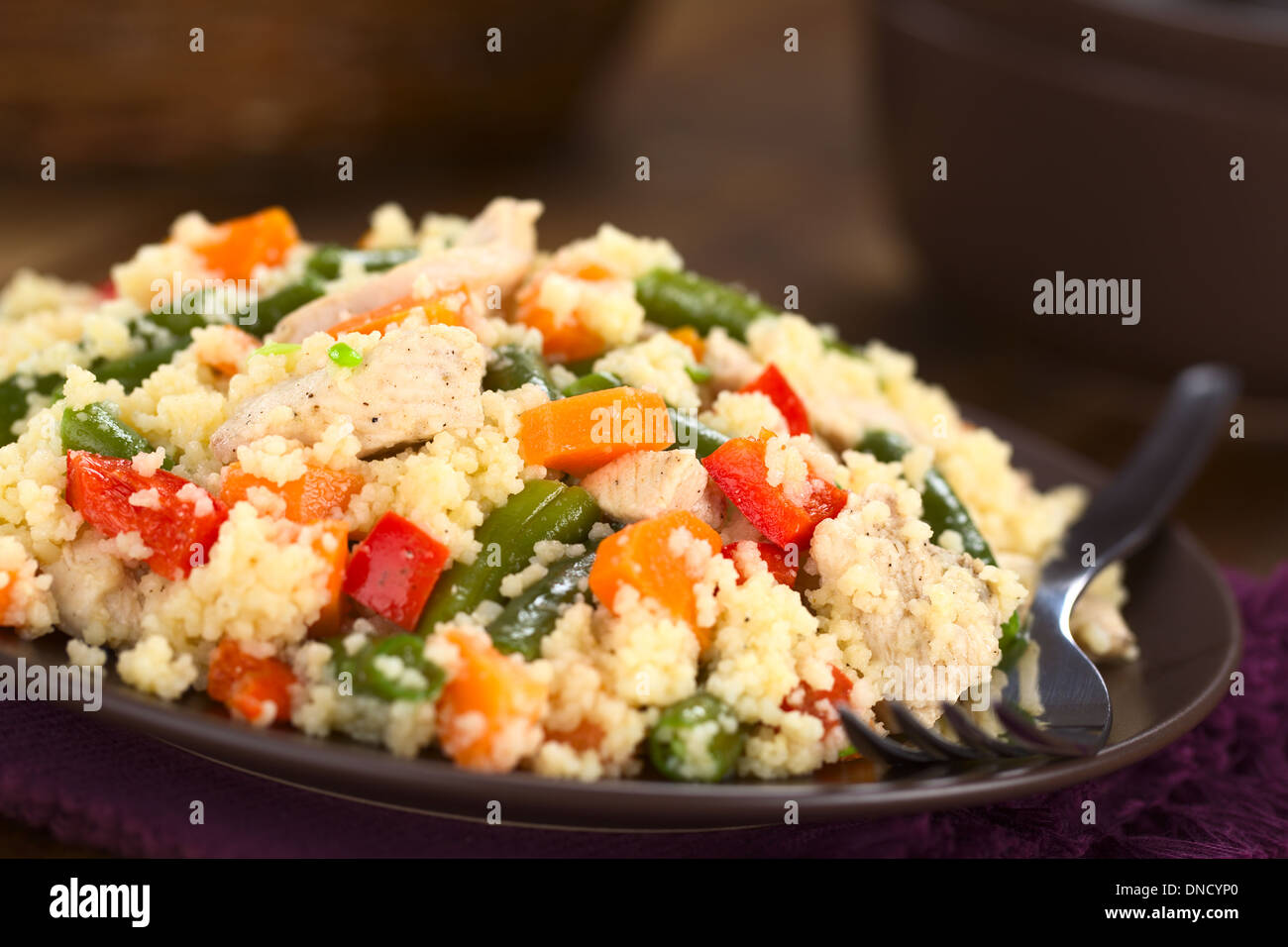 Il cous cous il piatto con il pollo, fagiolo verde, la carota e il peperone rosso servito sulla piastra con la forcella sul lato Foto Stock