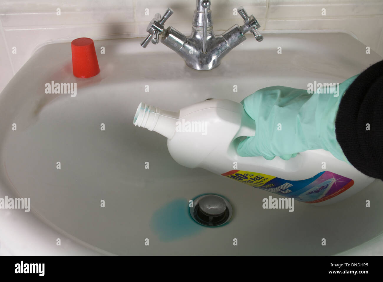 Close up donna verde da indossare guanti per la casa in possesso di una bottiglia di detergente liquido per mano bianca vasca in bagno Foto Stock