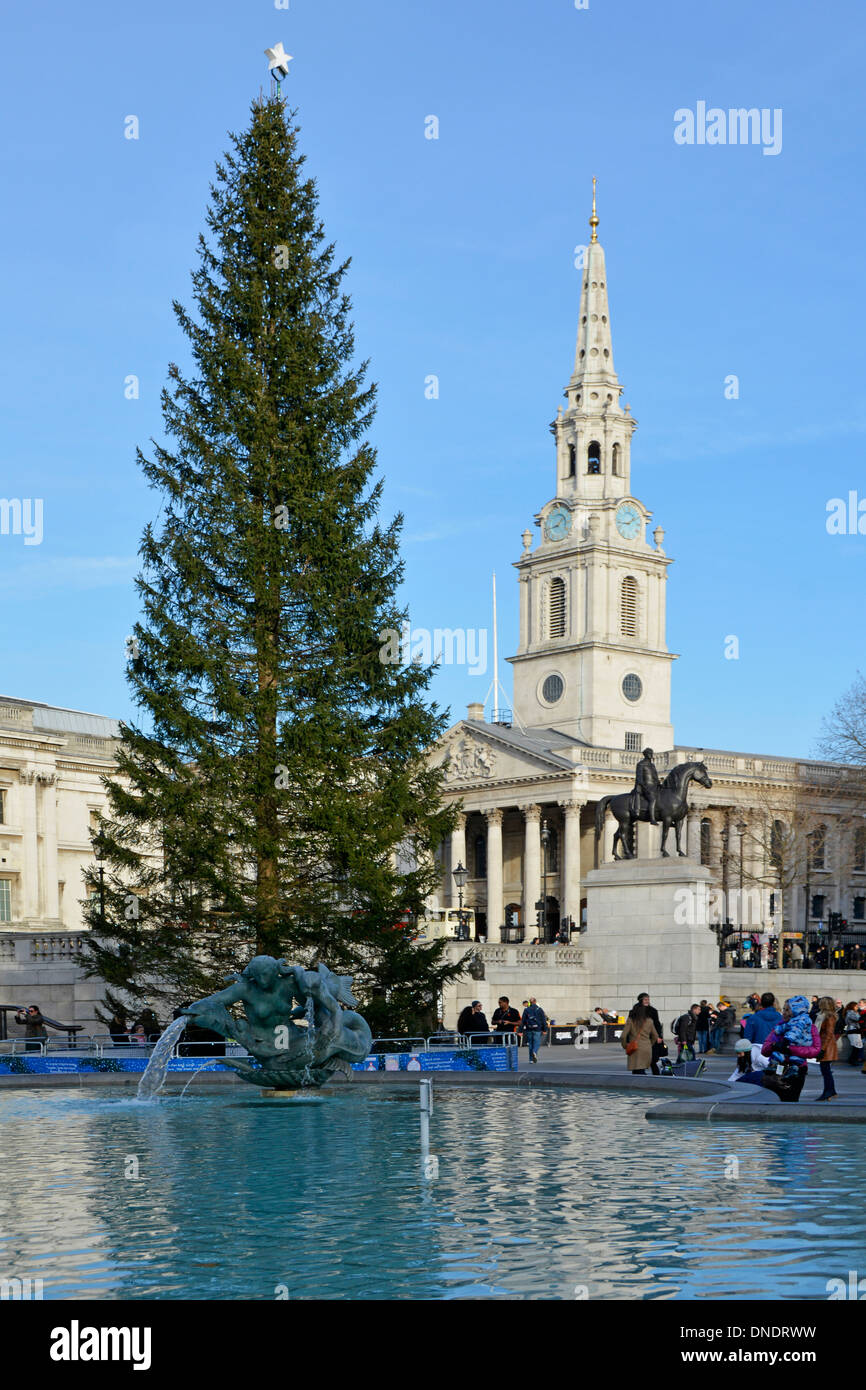 Albero di Natale & turisti in Trafalgar Square con St Martin nei campi guglia della chiesa al di là su un cielo blu gli inverni di giorno in Londra England Regno Unito Foto Stock