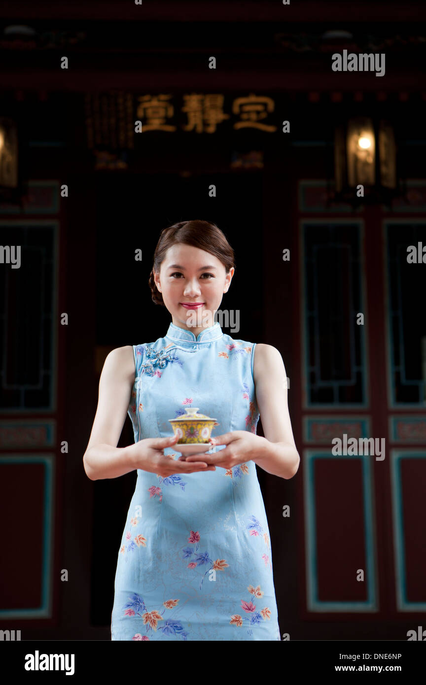 Giovane donna indossa cheongsam e titolari di una tazzina con il sorriso Foto Stock