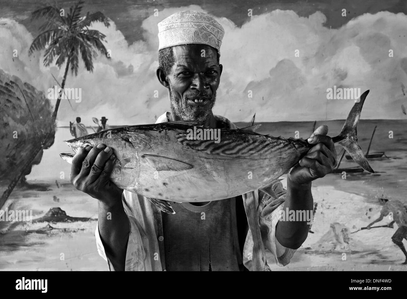 Un pescatore tiene un pesce tonno mentre si trova accanto ad un muro dipinto nell'isola di Zanzibar, una parte semi-autonoma della Tanzania, in Africa orientale Foto Stock