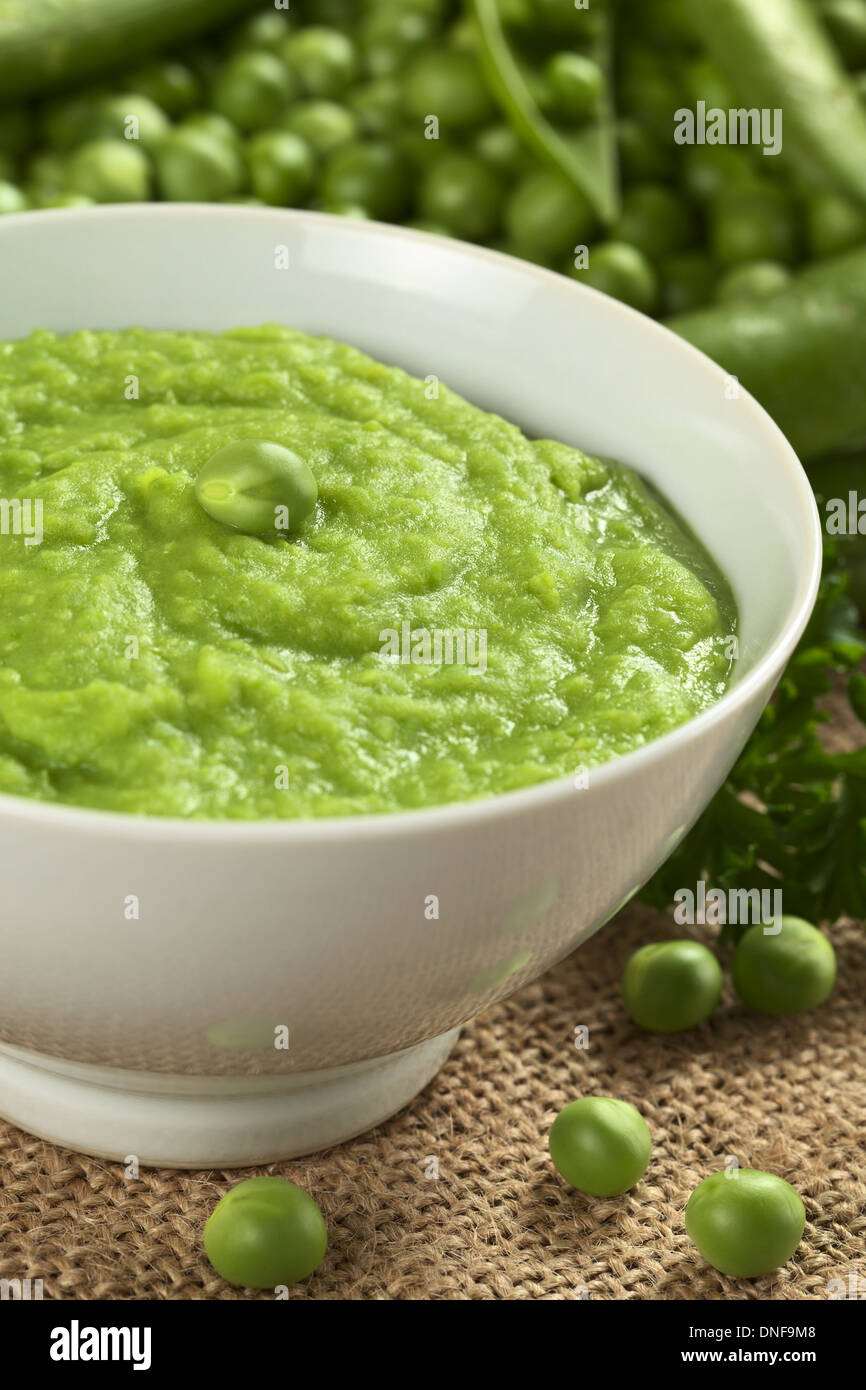 Fresco verde zuppa di piselli con i semi di pisello e baccelli di piselli intorno (messa a fuoco selettiva, focus sui piselli in mezzo alla minestra) Foto Stock