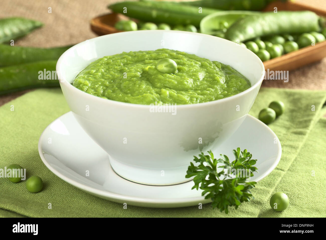 Fresco verde zuppa di piselli con i semi di pisello e baccelli di piselli intorno (messa a fuoco selettiva, focus sui piselli in mezzo alla minestra) Foto Stock