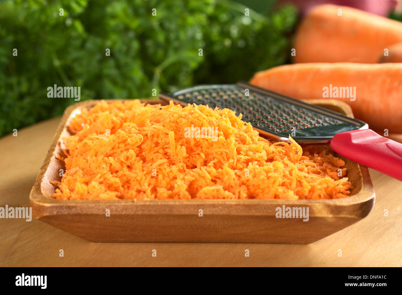 Freschi carote grattugiate nella ciotola di legno con grattugia (messa a fuoco selettiva, messa a fuoco sulla parte superiore del palo) Foto Stock