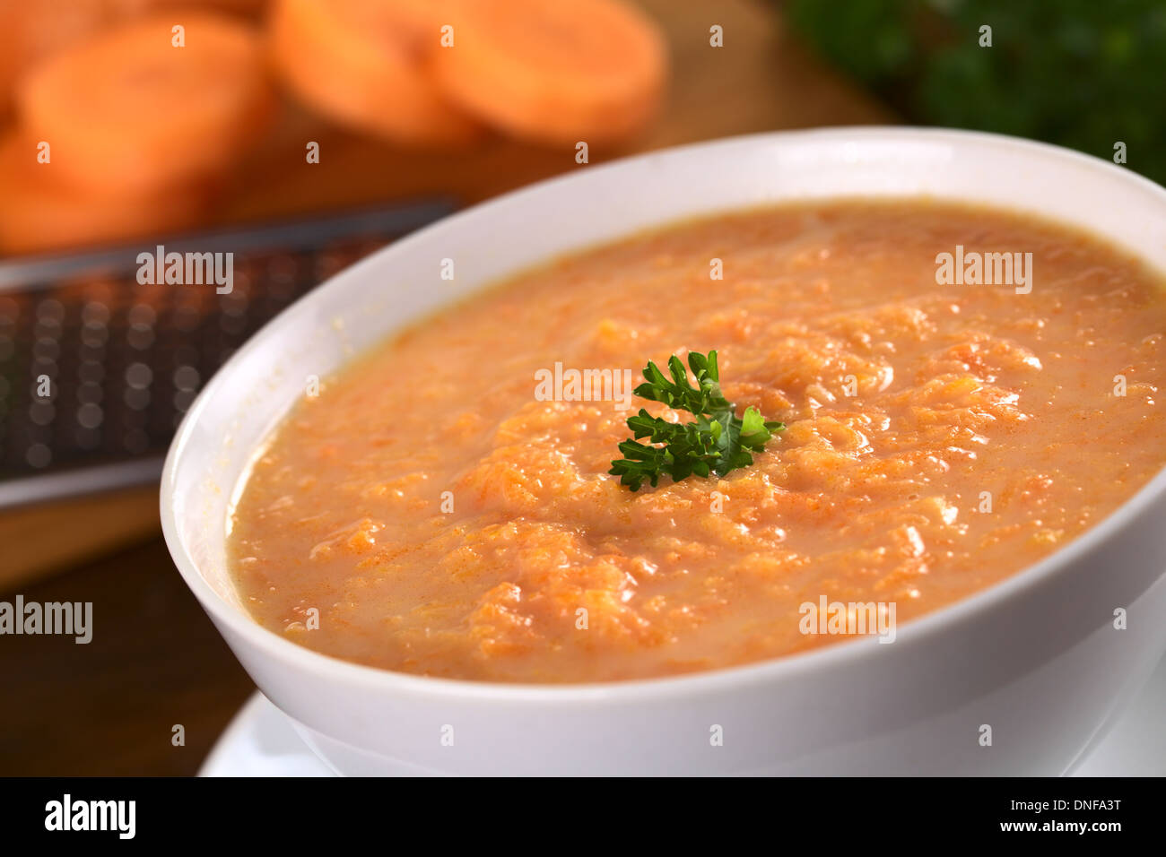 La carota crema zuppa di carote grattugiate e guarnito con una foglia di prezzemolo (messa a fuoco selettiva, concentrarsi sulle foglie di prezzemolo) Foto Stock