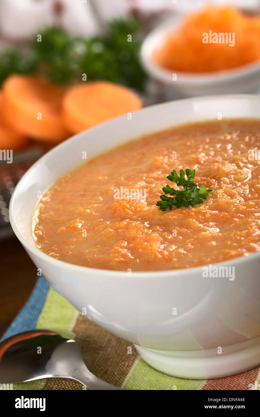 La carota crema zuppa di carote grattugiate e guarnito con una foglia di prezzemolo (messa a fuoco selettiva, concentrarsi sulle foglie di prezzemolo) Foto Stock