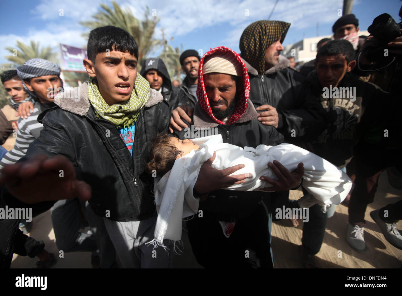 La striscia di Gaza, Territori palestinesi. 25 Dic, 2013. Un mourner porta il corpo di una ragazza palestinese all'età di tre anni alo Bhairi, che i medici hanno detto è stato ucciso da schegge da un attacco aereo israeliano, in un cimitero nella zona centrale della striscia di Gaza il 25 dicembre 2013. Un cecchino ha ucciso un civile israeliana sulla frontiera Gaza martedì e Israele ha risposto con attacchi aerei su due campi di addestramento di Hamas, che ospedale funzionari detti ucciso una ragazza palestinese vicino a uno degli obiettivi.Foto: Majdi Fathi/NurPhoto Credito: Majdi Fathi/NurPhoto/ZUMAPRESS.com/Alamy Live News Foto Stock