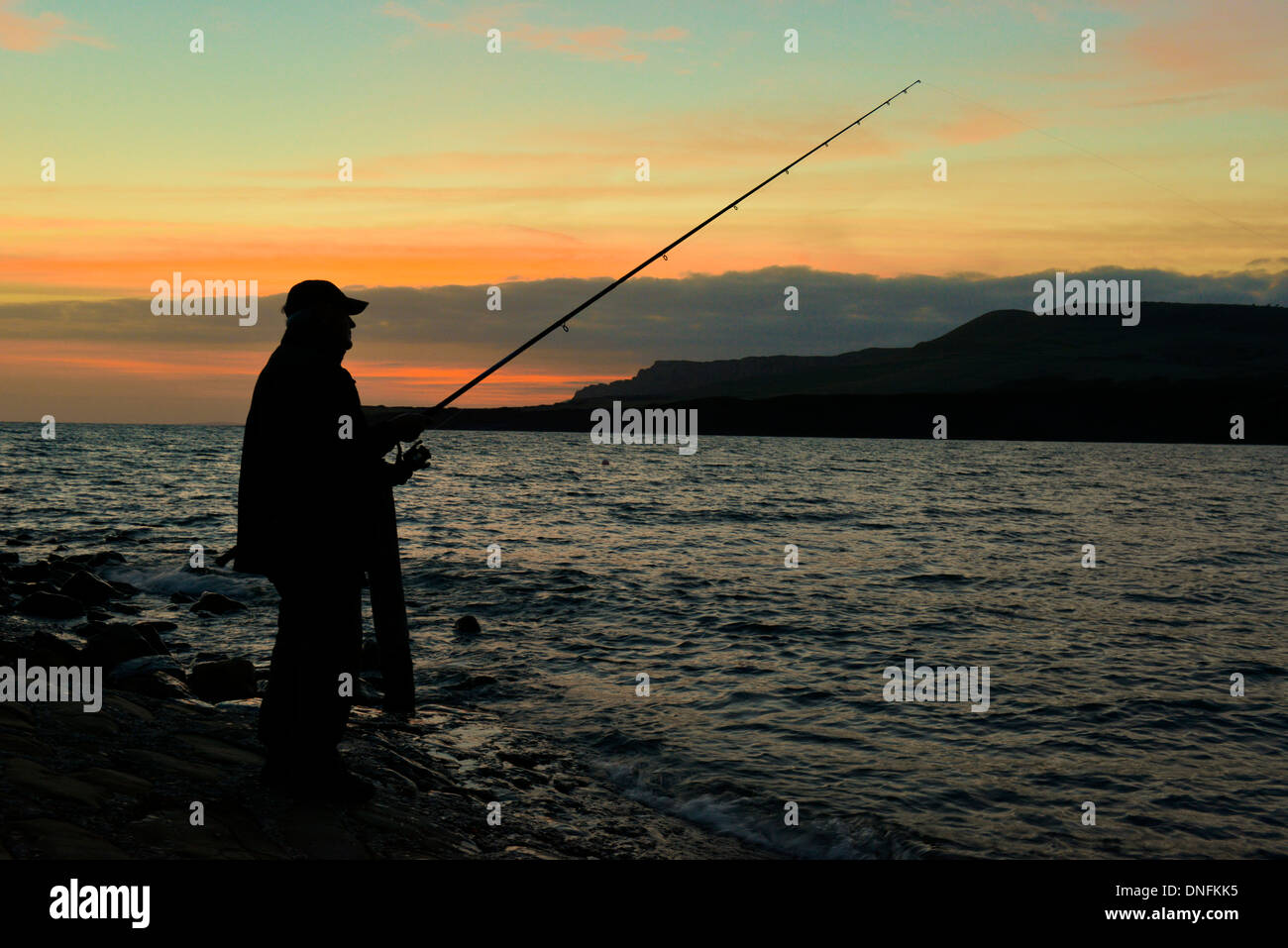 Il pescatore con attività di pesca nell'ultima luce della sera a Kimmeridge Bay, Dorset Foto Stock