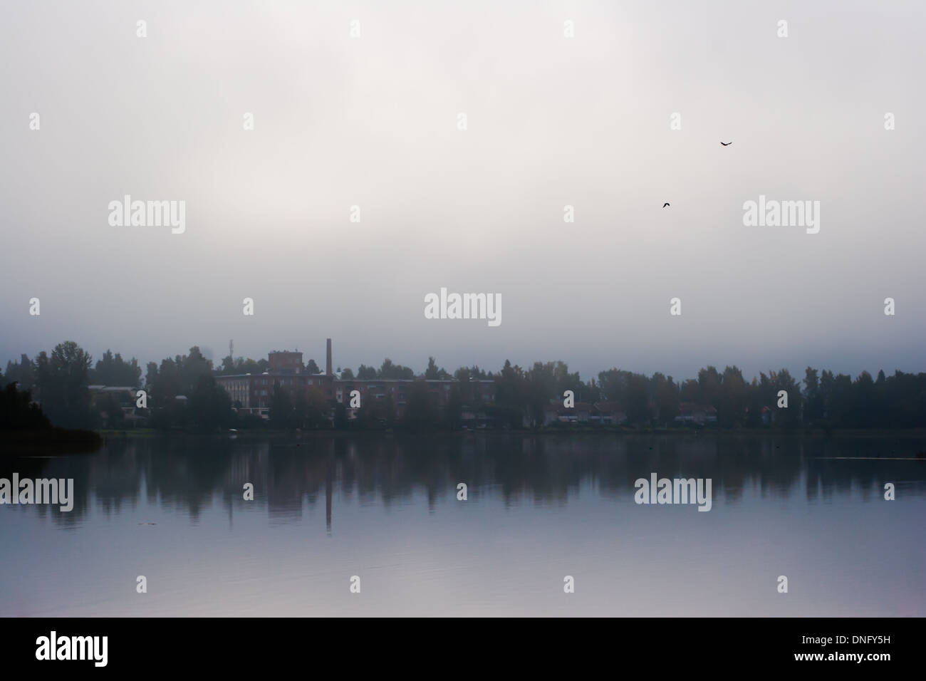 Piccola città dietro un lago su nebbiosa mattina nuvoloso Foto Stock