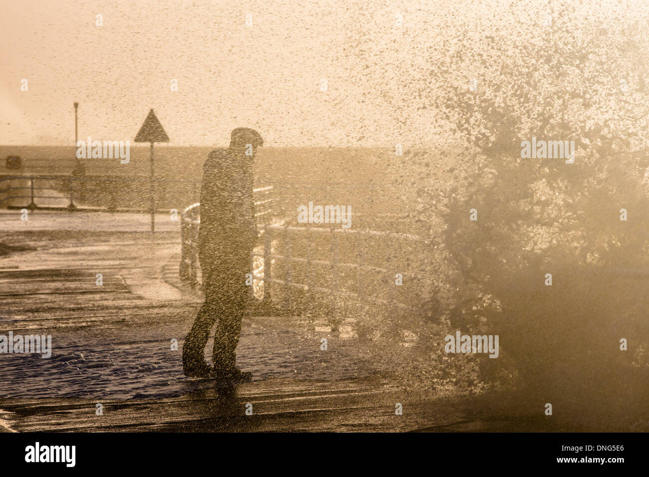 Aberystwyth, Wales, Regno Unito. Il 27 dicembre 2013. Gale force venti pastella la costa gallese e ad alta marea massiccia onde si infrangono sul fronte mare a Aberystwyth. Panna montata in schiuma dal vento che copre la spiaggia e il lungomare Sud come sta un uomo in silhouette contro il sole di setting, guardando la rottura a spruzzo sopra il mare di ringhiere. Credito: atgof.co/Alamy Live News Foto Stock