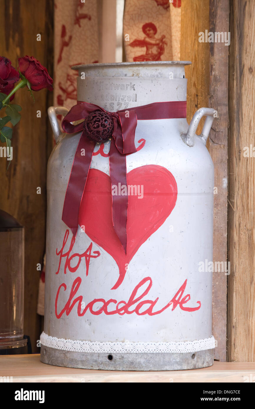 White bidone di latte con un cuore rosso e nastro con le parole di cioccolato caldo su di esso Foto Stock