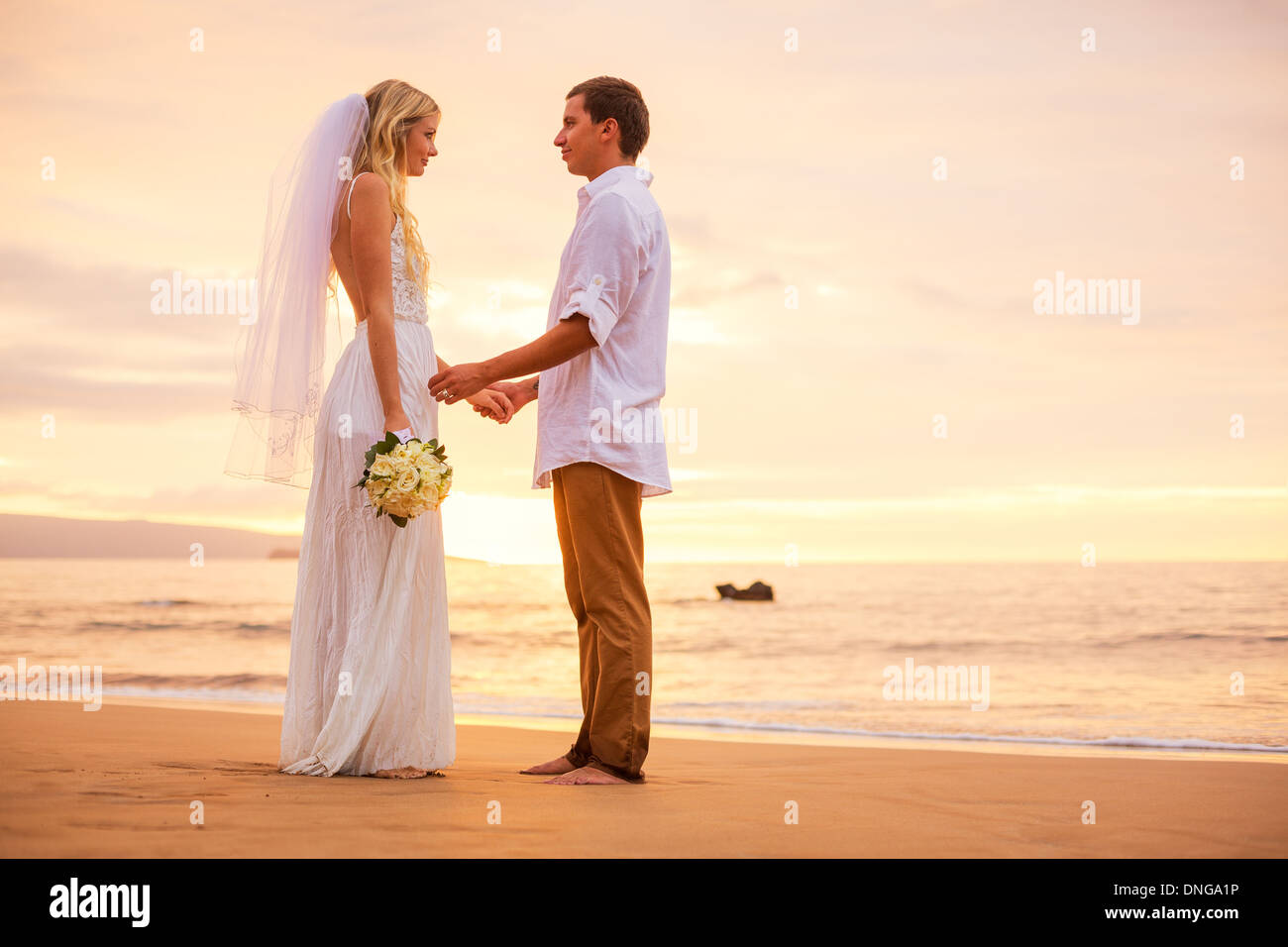 Appena una coppia sposata tenendo le mani sulla spiaggia al tramonto, Hawaii matrimonio sulla spiaggia Foto Stock