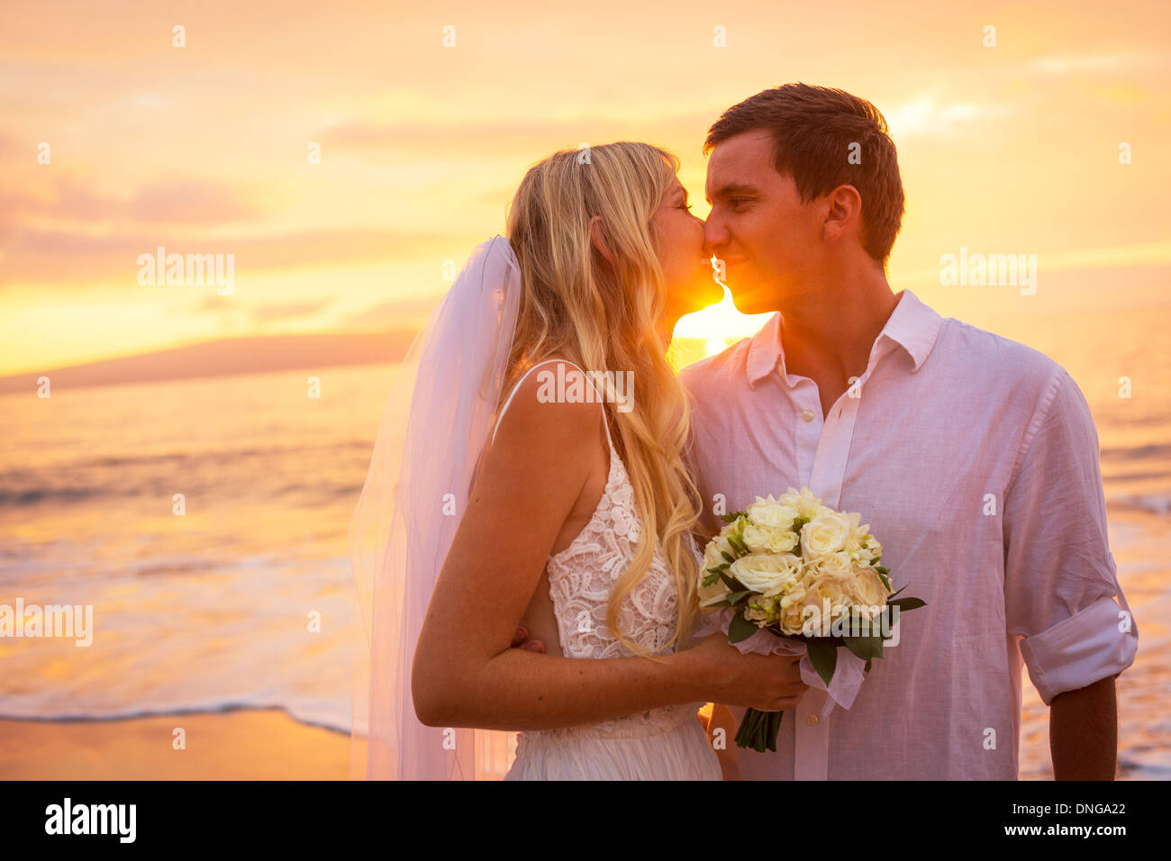 Appena una coppia sposata baciare sulla spiaggia tropicale al tramonto, Hawaii matrimonio sulla spiaggia Foto Stock