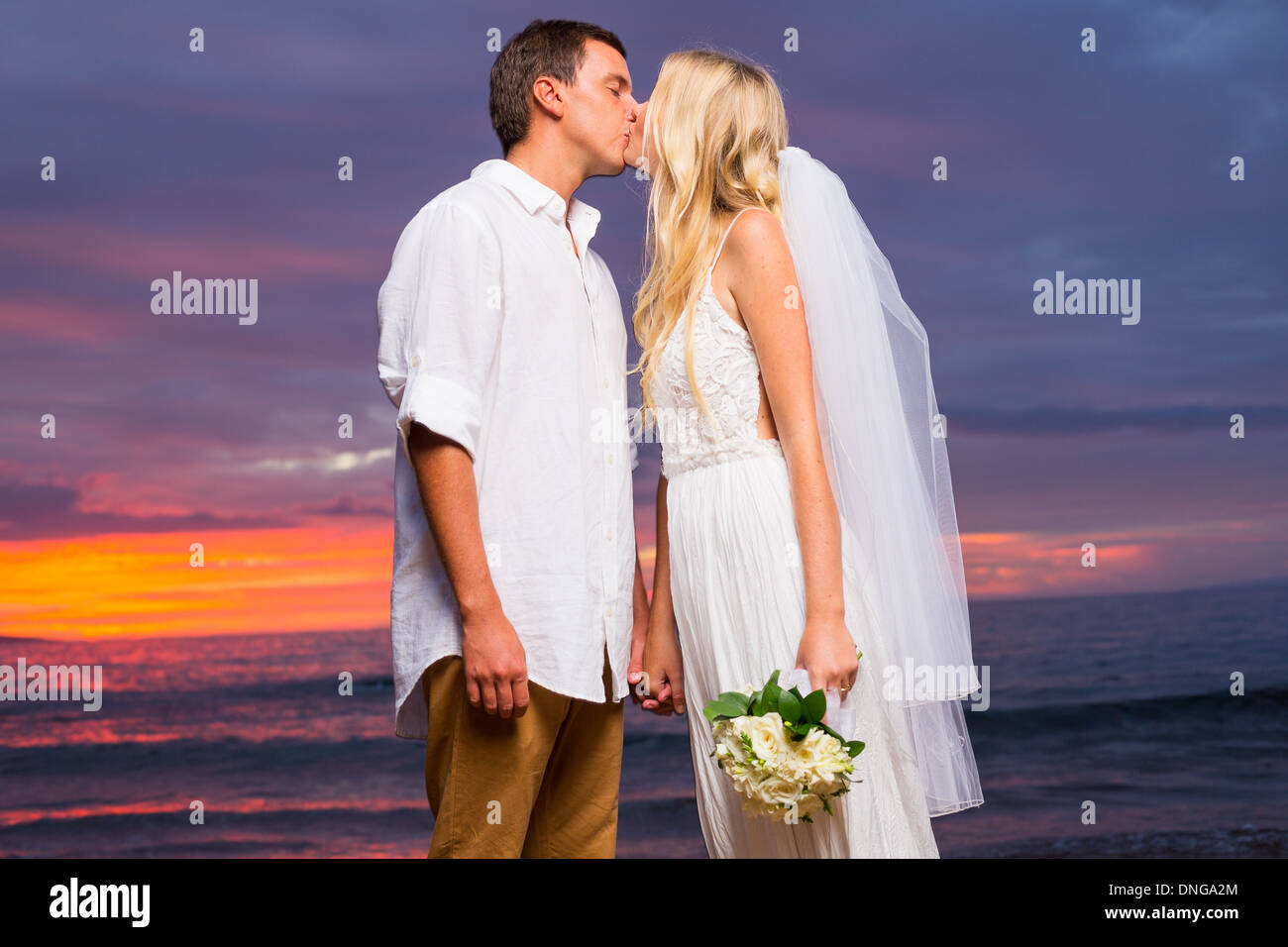 Appena una coppia sposata baciare sulla spiaggia tropicale al tramonto, Hawaii matrimonio sulla spiaggia Foto Stock