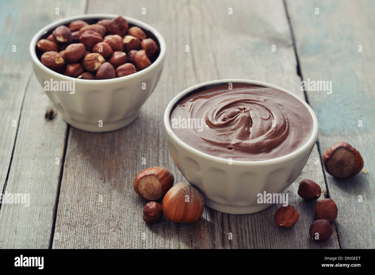 Crema nocciola nella ciotola in ceramica con nocciole su sfondo di legno Foto Stock