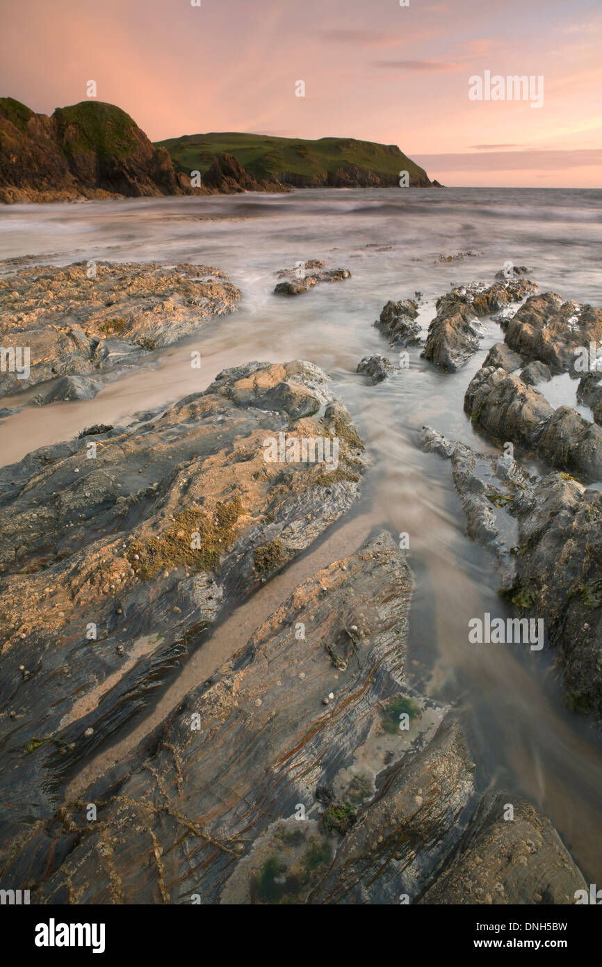 La marea di bobine in oltre le rocce sulla spiaggia a Hope Cove, Devon. Il sunrise getta una luce calda oltre il paesaggio e il mare. Foto Stock